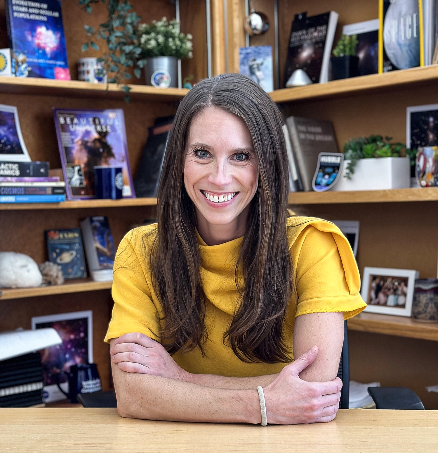 A woman is sitting at a table in front of a bookshelf.