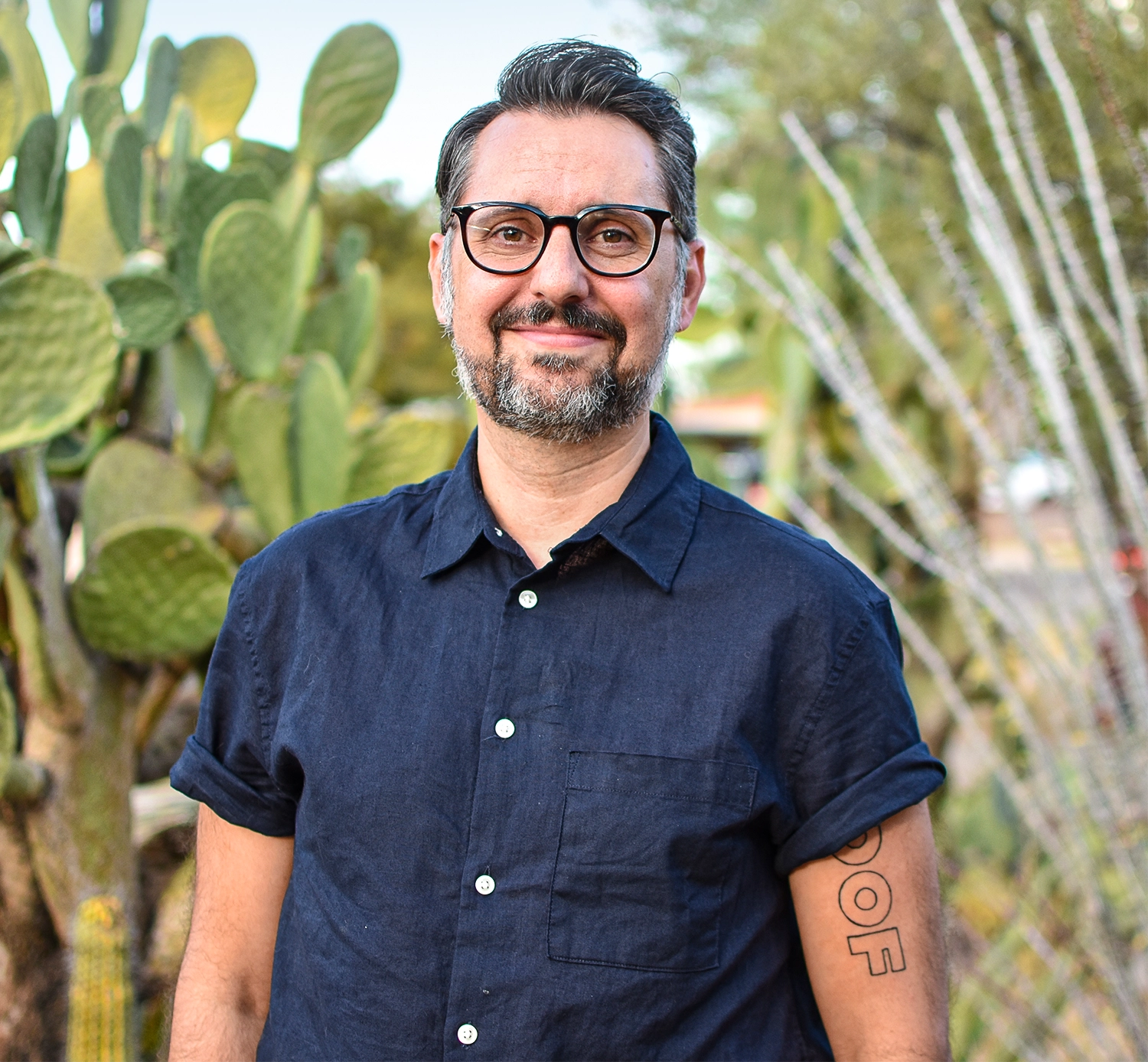 A man with glasses and a beard is standing in front of a cactus.